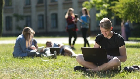 Young students hanging out on a campus meadow.