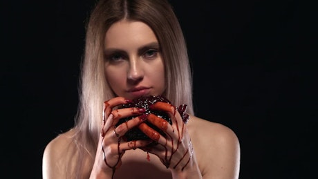 Young woman biting into a bloody heart.