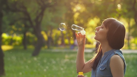 Young woman blowing bubbles in a park at sunset