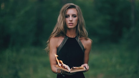 Young woman burning a book outdoors.