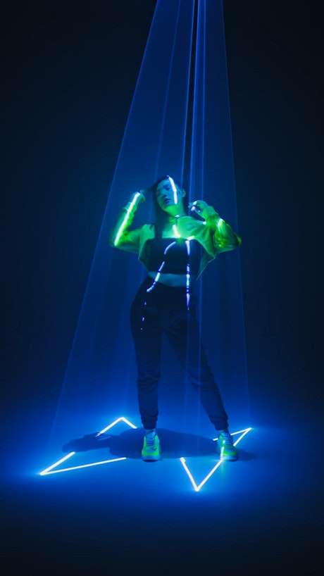 Young woman dances and moves slowly underneath green neon lights.
