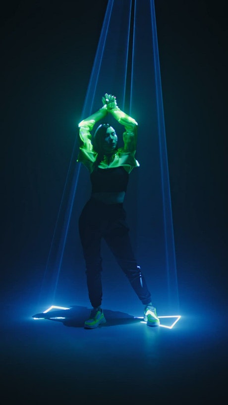 Young woman dances and moves slowly underneath laser lights.