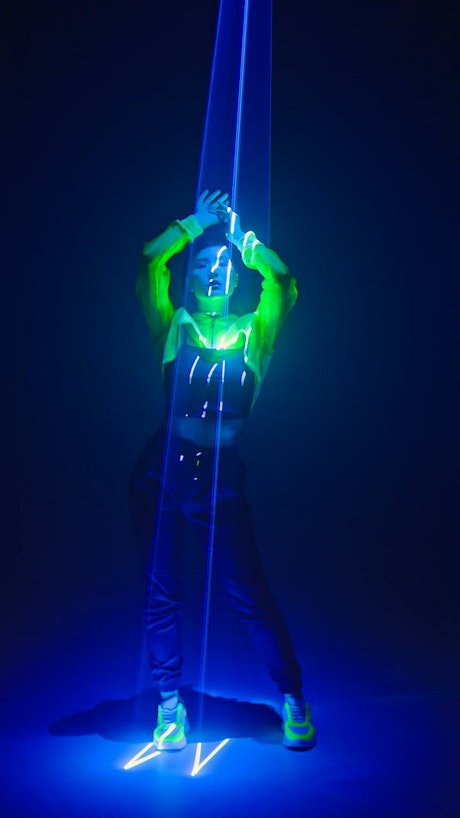Young woman dances and moves slowly underneath neon lights.