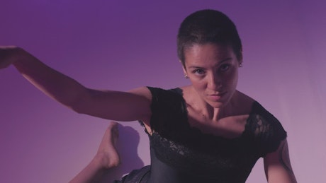 Young woman dancing sitting on the floor on lilac background.