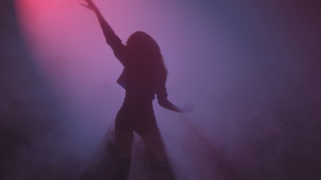 Young woman dancing under a cloud of smoke and a purple light.