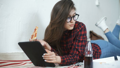 Young woman eating pizza and relaxing with tablet.