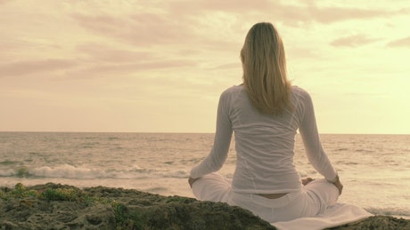 Young woman in white is meditating on a beach.