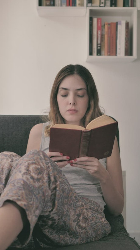 Young woman lying on a sofa reading a book.