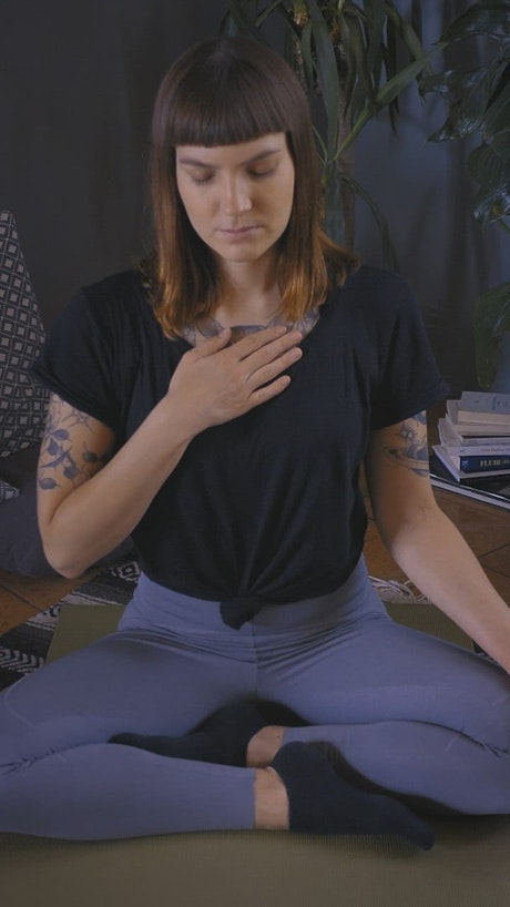 Young woman meditating on the floor with hand on chest.