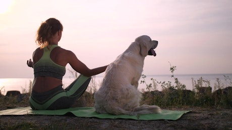 Young woman meditating with her dog aside near sea.