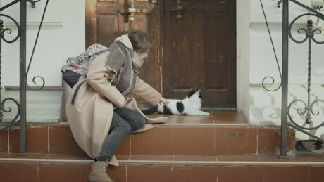 一个年轻的女人在一所房子的台阶上和一只小猫玩耍