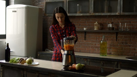 Young woman preparing a smoothie in a kitchen.