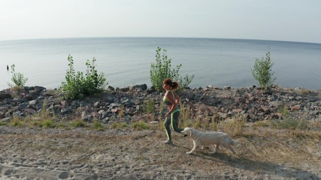 Young woman running with her dog near a coast.