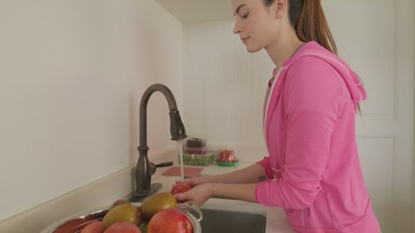Young woman washing fruit in her kitchen.