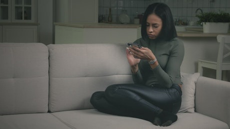 Young woman watching her phone in the couch.