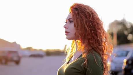 Young woman with long red hair embraces the sunshine.