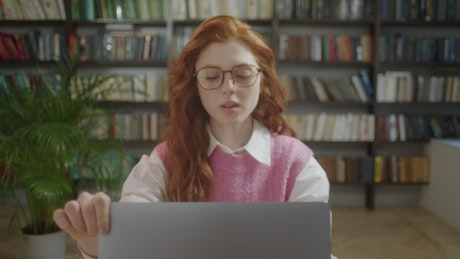 Young woman with red hair sitting on a table at the library.